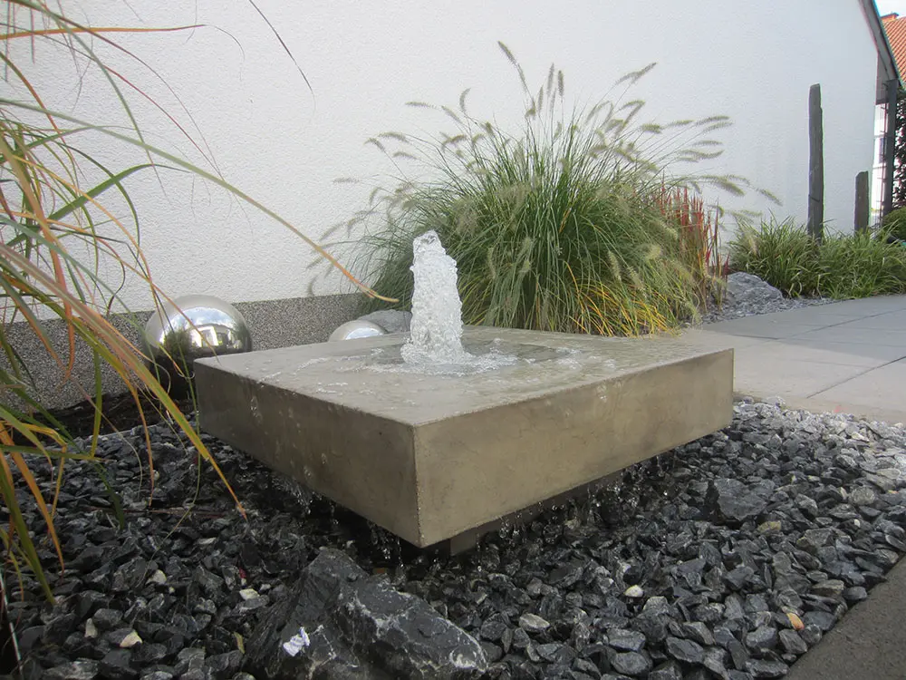 Moderner Gartenspringbrunnen in Betonoptik und großer Fontäne