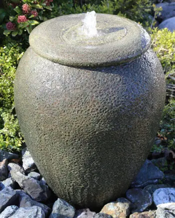 Palermo Keramik-Springbrunnen in antiker Krugform mit sprudelndem Wasser, umgeben von grünen Pflanzen und Steinen in einem Garten.