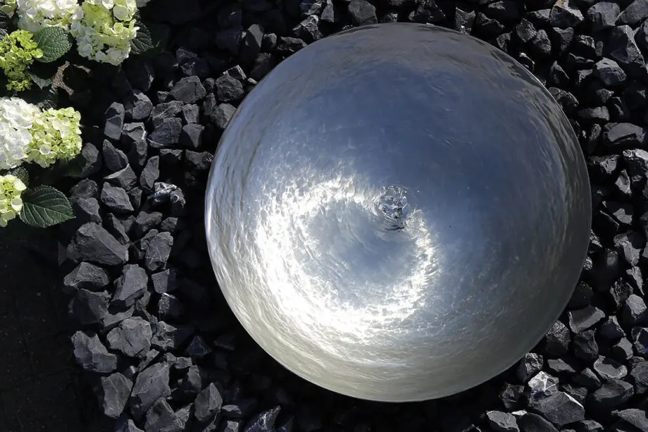 Edelstahl-Wasserschale Modell 2396 mit leicht gewellter Wasseroberfläche, aufgestellt auf einer Terrasse mit dunklen Steinplatten, umgeben von modernen Pflanzen.