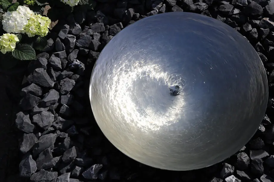 Edelstahl-Wasserschale Modell 2396 mit leicht gewellter Wasseroberfläche, aufgestellt auf einer Terrasse mit dunklen Steinplatten, umgeben von modernen Pflanzen.