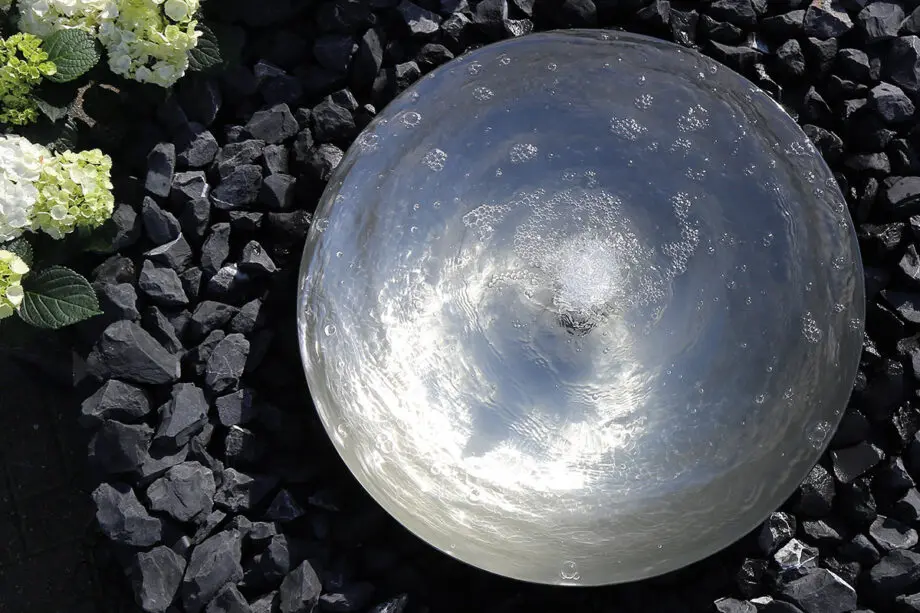 Edelstahl-Wasserschale Modell 2396 mit leicht gewellter Wasseroberfläche, aufgestellt auf einer Terrasse mit dunklen Steinplatten, umgeben von modernen Pflanzen.