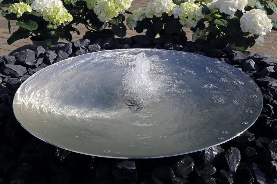 Edelstahl-Wasserschale Modell 2396 mit leicht gewellter Wasseroberfläche, aufgestellt auf einer Terrasse mit dunklen Steinplatten, umgeben von modernen Pflanzen.