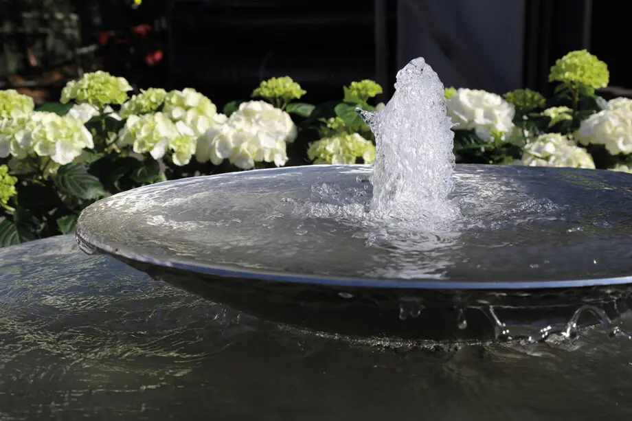 Edelstahl-Schale Duo mit zwei Wasserschalen (100 cm und 60 cm Ø), Sprudelquell in der oberen Schale, aufgestellt in einem modernen Garten mit Kies und Pflanzen.