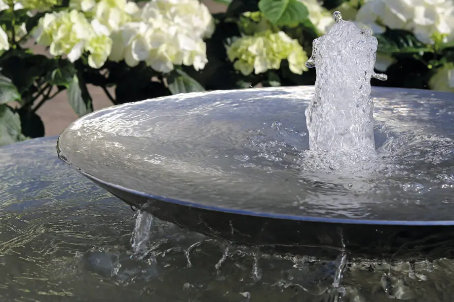 Edelstahl-Schale Duo mit zwei Wasserschalen (100 cm und 60 cm Ø), Sprudelquell in der oberen Schale, aufgestellt in einem modernen Garten mit Kies und Pflanzen.