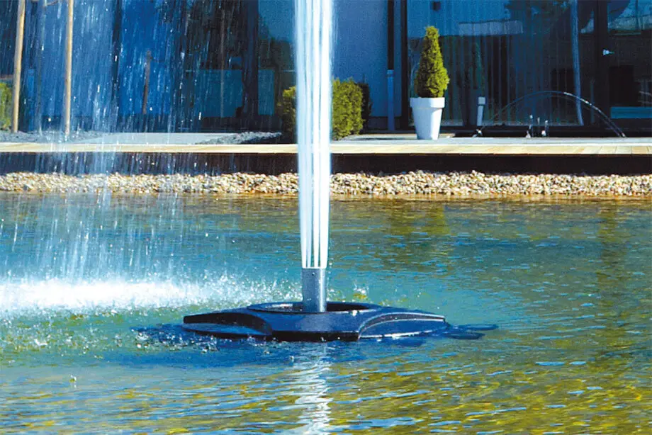 Oase Geyser Jet 30 auf einer Schwimmfontäne Profi in einem Teich, mit einem 5 m hohen, breiten Wasserstrahl aus Edelstahldüse, umgeben von grünen Uferpflanzen.