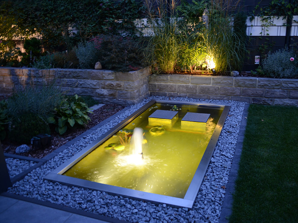 Rechteckiges Teichbecken mit Trittstufen und großer Schaumfontäne als ...