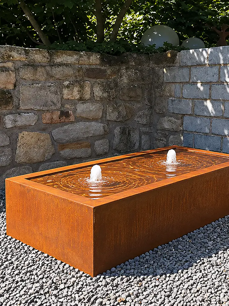 Rechteckiger Cortenstahl-Wassertisch in warmem Edelrost mit zwei sprudelnden Wasseraustritten im Garten