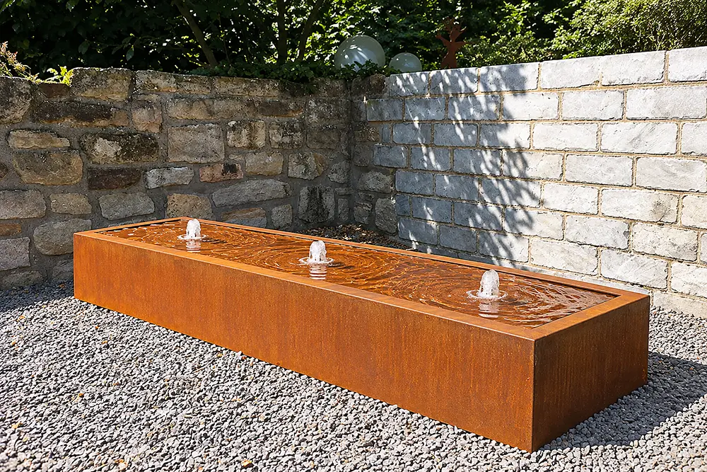 Rechteckiger Cortenstahl-Wassertisch in warmem Edelrost mit zwei sprudelnden Wasseraustritten im Garten